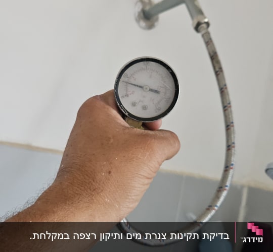 מד לחץ מים מוחזק ביד ליד מקלחת